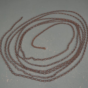 May include: A long, coiled chain made of metal links. The chain is rusty brown in color and appears to be made of iron.
