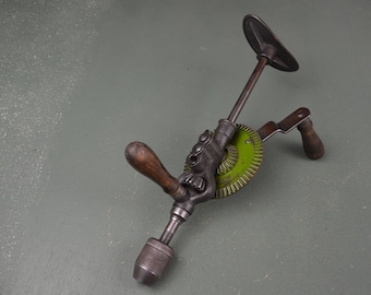 May include: A vintage hand drill with a green gear and wooden handles. The drill is made of metal and has a black finish.
