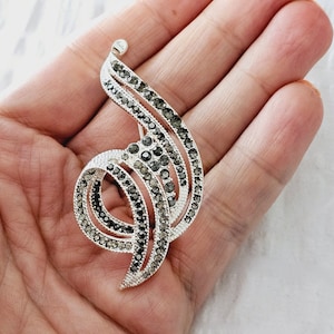 Puede incluir: Un broche de plata con un diseño de espiral, adornado con diamantes de imitación negros.