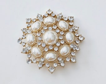 Könnte beinhalten: Eine goldfarbene Brosche mit einem Sternendesign, das mit einer Ansammlung von Kunstperlen und klaren Strasssteinen verziert ist.