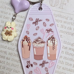 May include: A lavender keychain with a metal ring, a heart charm, and a bunny charm. The main charm is a lavender motel-style tag with coffee cup illustrations and the word "coffee".