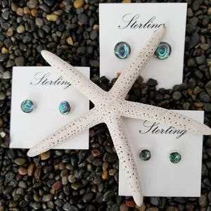 May include: Three pairs of sterling silver earrings with abalone shell inlays. The earrings are displayed on white cards with the word "Sterling" printed on them.