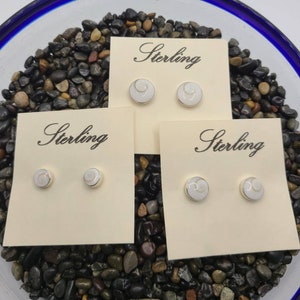 Może przedstawiać: Trzy pary kolczyków ze srebra próby 925 z białą wkładką z muszli. Każda para jest prezentowana na małej kartce z nadrukiem "Sterling".