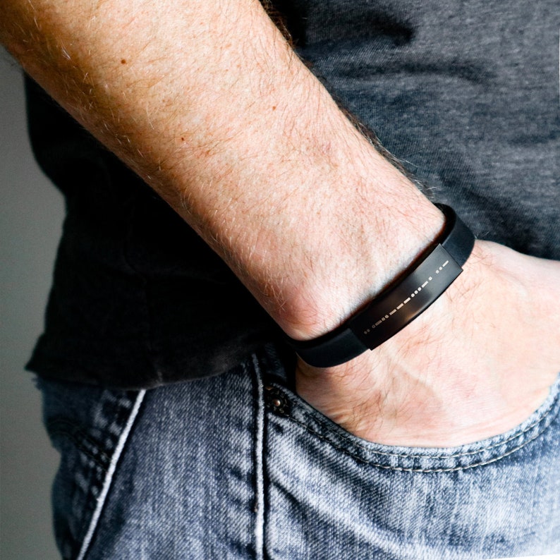 Puede incluir: Una pulsera de silicona negra con una inscripci&oacute;n en braille plateada.
