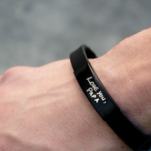 Puede incluir: Una pulsera de silicona negra con las palabras "Love you, Papa" grabadas en blanco.