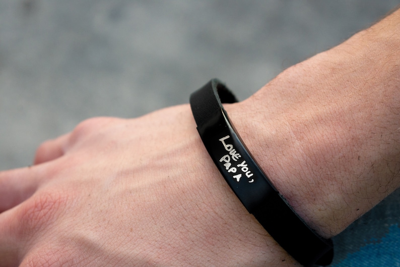 Puede incluir: Una pulsera de silicona negra con las palabras "Love you, Papa" grabadas en blanco.