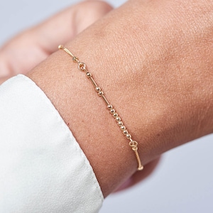 May include: A delicate gold bracelet with small beads, worn on a wrist.