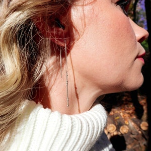 May include: A pair of silver dangle earrings with small beads on a thin chain.