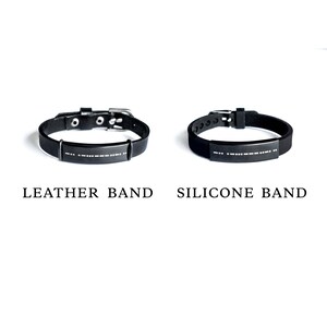 Puede incluir: Dos pulseras negras con una hebilla plateada y una placa plateada con letras en braille. La pulsera de la izquierda es una banda de cuero y la pulsera de la derecha es una banda de silicona.