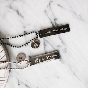 Può includere: Due collane d'argento con ciondoli incisi personalizzati. Un ciondolo recita "Love You! Mom" e l'altro "Love, Mama". Una collana ha un ciondolo d'argento con un simbolo dei Pesci.