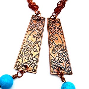 Peut inclure: Une paire de boucles d'oreilles en cuivre avec une perle turquoise pendante. Le cuivre est gravé d'un motif floral et les boucles d'oreilles sont attachées à un crochet argenté.