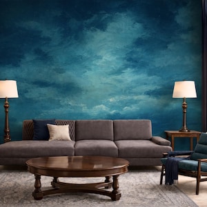 May include: A living room scene featuring a dark gray sofa with accent pillows, a round wooden coffee table, and a teal armchair. The backdrop is a large wall mural with a blue and teal cloud-like design. Two lamps flank the sofa.