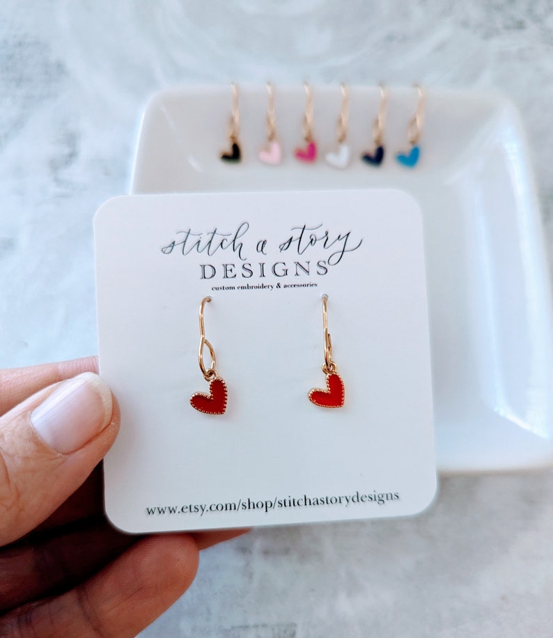 May include: Red heart dangle earrings with gold hooks. The earrings are on a white card with the text "stitch a story DESIGNS custom embroidery & accessories www.etsy.com/shop/stitchastorydesigns"