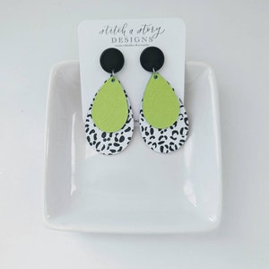 May include: A pair of dangle earrings with a green and black and white leopard print design. The earrings are made of leather and have black round tops.