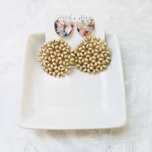 Peut inclure: Une paire de boucles d'oreilles avec un groupe de perles rondes en bois beige et un pendentif en r&eacute;sine translucide multicolore en demi-cercle. Les boucles d'oreilles sont sur une plaque carr&eacute;e blanche avec le texte "stitch a story" sur une carte blanche derri&egrave;re elles.