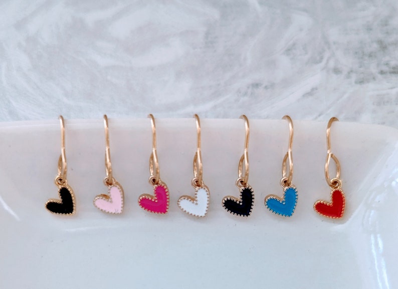 May include: Seven pairs of gold heart-shaped earrings with different coloured enamel. The colours are black, pink, red, white, blue, and two shades of pink.