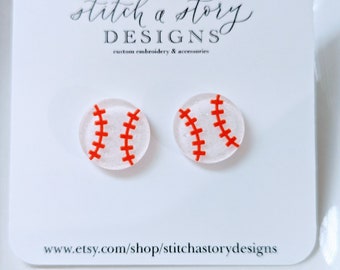 Peut inclure: Une paire de boucles d'oreilles de baseball blanches avec des coutures rouges. Les boucles d'oreilles sont en résine et ont une finition pailletée. Les boucles d'oreilles sont sur une carte blanche avec le texte "stitch a story DESIGNS broderie personnalisée & accessoires www.etsy.com/shop/stitchastorydesigns".