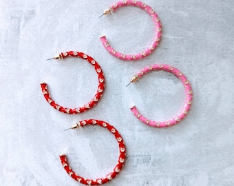 Op de afbeelding: Drie paar creolen met een hartvormig patroon. Een paar is rood, een paar is roze en een paar is een mix van rood en roze.