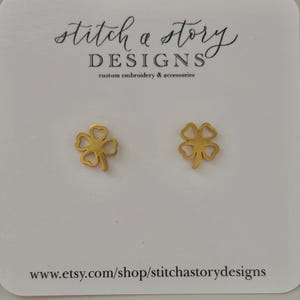 May include: Gold four-leaf clover earrings on a white card with the text "stitch a story DESIGNS custom embroidery & accessories www.etsy.com/shop/stitchastorydesigns"