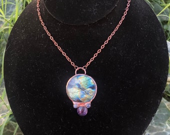 May include: A copper chain necklace with a round pendant featuring a blue, green, and gold iridescent stone. The pendant is accented with two small purple stones.