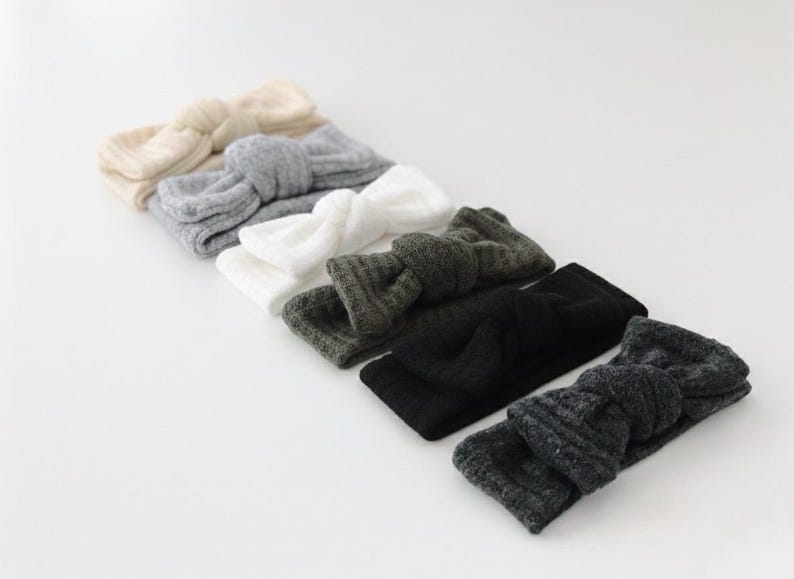 Puede incluir: Una colecci&oacute;n de seis diademas de punto en varios colores. Las diademas est&aacute;n dispuestas en fila, mostrando tonos crema, gris, blanco, verde oscuro, negro y gris carb&oacute;n. Cada diadema presenta un dise&ntilde;o de lazo anudado.
