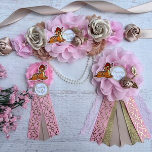 May include: Pink and gold mommy-to-be and daddy-to-be sashes with a floral design and a cartoon Bambi. The sashes have the text "Mommy to Be" and "Daddy to Be" printed on them.