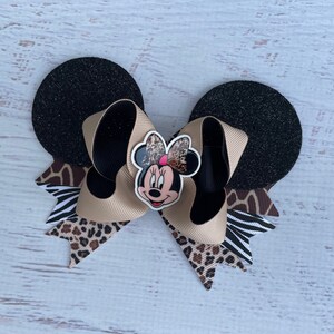 May include: A black and brown Minnie Mouse bow with a cheetah, zebra, and leopard print. The bow is attached to black glitter mouse ears.