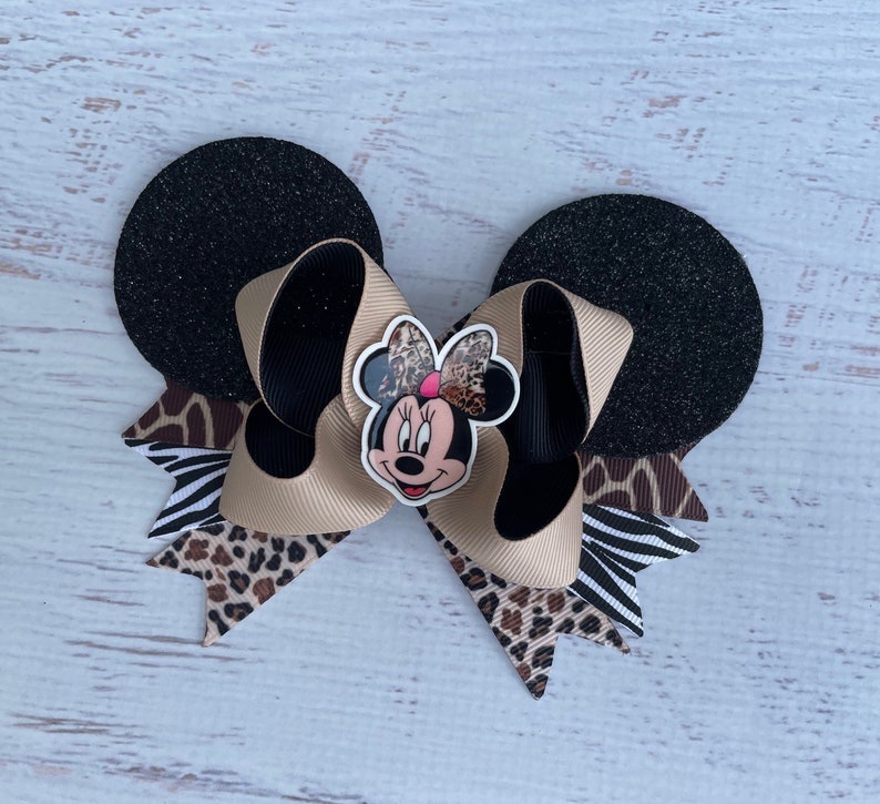 May include: A black and brown Minnie Mouse bow with a cheetah, zebra, and leopard print. The bow is attached to black glitter mouse ears.