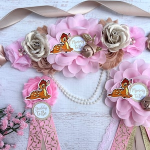 May include: Pink and gold floral sash with a Bambi character and the text "Mommy To Be".  Two matching sashes with the text "Daddy To Be" and "Mommy To Be" are also included.