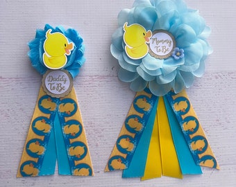 May include: Two blue and yellow baby shower sashes with rubber ducky designs. One sash says "Mommy To Be" and the other says "Daddy To Be".