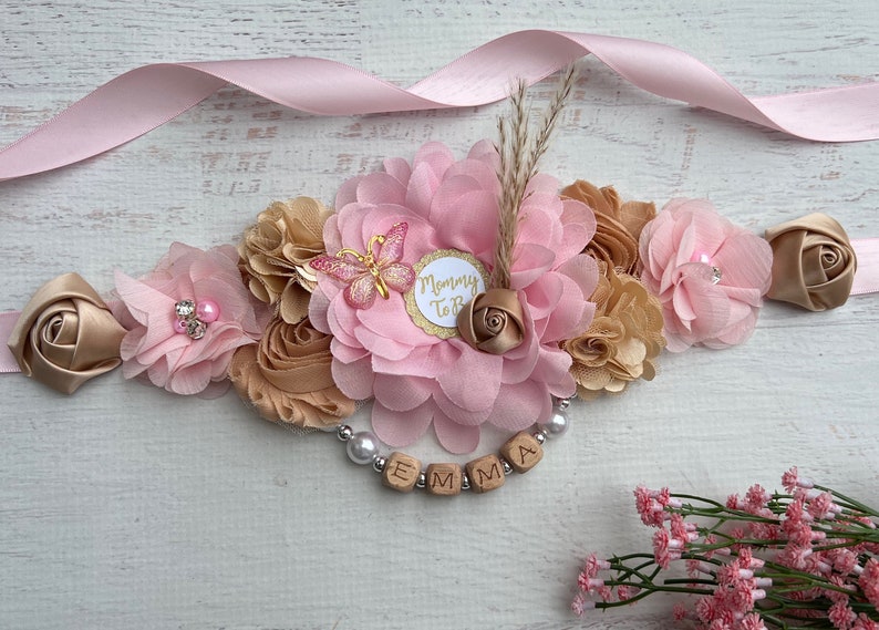 May include: A pink and gold floral sash with a "Mommy To Be" badge and a wooden name tag that reads "EMMA".