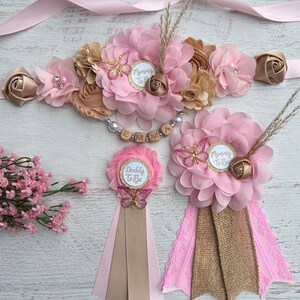 May include: Pink and gold floral sashes with the text "Mommy to Be" and "Daddy to Be" and a matching flower crown with the name "Emma" spelled out in wooden beads.