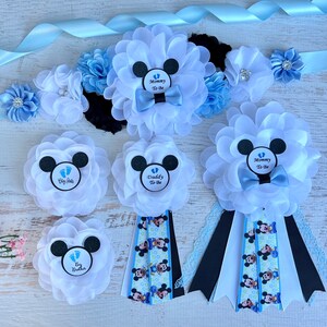 May include: A set of five blue and white Mickey Mouse themed baby shower sashes. The sashes feature a black Mickey Mouse head with a blue bow tie and the text "Mommy To Be", "Daddy To Be", and "Big Brother".