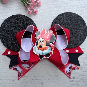 May include: Red and white bow with black polka dots and a Minnie Mouse character in the centre. The bow is attached to two black felt mouse ears.