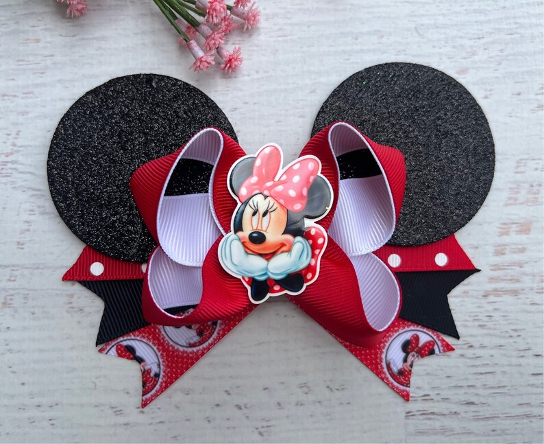 May include: Red and white bow with black polka dots and a Minnie Mouse character in the centre. The bow is attached to two black felt mouse ears.