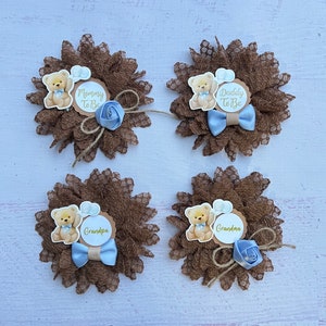 May include: Four brown lace flower pins with a teddy bear and text. The pins say "Mommy to Be", "Daddy to Be", "Grandma", and "Grandpa".