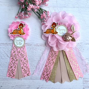 May include: Two pink and gold baby shower sashes with a cartoon Bambi design. The sashes have the text 'Mommy to Be' and 'Daddy to Be' on them