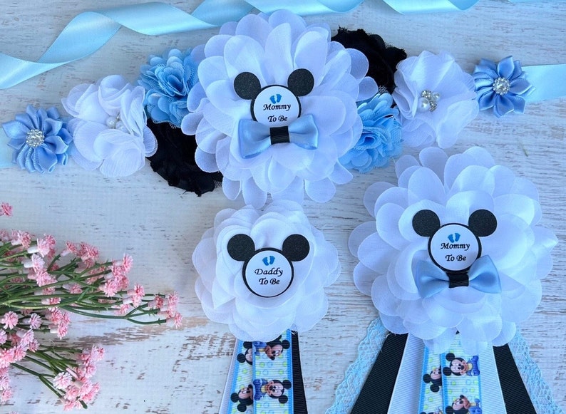 May include: Three blue and white flower sashes with black ribbon and Mickey Mouse ears. The sashes have the text "Mommy to Be" and "Daddy to Be" on them.