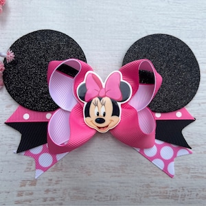 May include: Pink and black Minnie Mouse hair bow with black glitter ears and white polka dot accents.