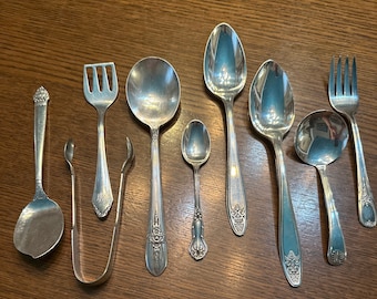 May include: A set of nine silver-plated utensils, including spoons, forks, and a serving spoon. The utensils have ornate designs and are in excellent condition.