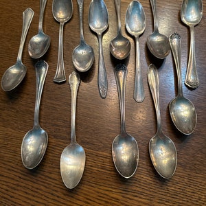 Puede incluir: Una colección de 13 cucharas de plata con mangos ornamentados. Las cucharas están dispuestas en dos filas sobre una superficie de madera.