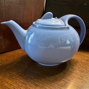 May include: A light blue ceramic teapot with a rounded body and a lid with a small knob. The teapot has a spout and a handle.