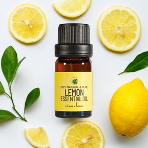 Puede incluir: Una pequeña botella de vidrio ámbar con una tapa negra y una etiqueta amarilla que dice "100% NATURAL & PURE LEMON ESSENTIAL OIL citrus x limon". La botella está rodeada de rodajas de limón y hojas verdes.