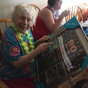 May include: A framed black chalkboard sign with gold glitter accents and white text celebrating a 90th birthday. The sign lists historical events and average costs from the year 1927. The sign is 16 inches by 20 inches.