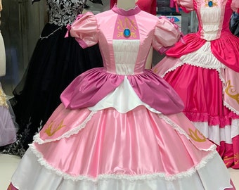 May include: A pink and white ball gown with a gold trim and a blue jewel on the bodice. The dress has a layered skirt with a white lace trim.