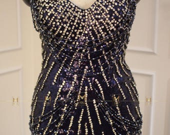 May include: A black sequined bodysuit with fringe detailing. The bodysuit has a sweetheart neckline and is adorned with silver sequins.