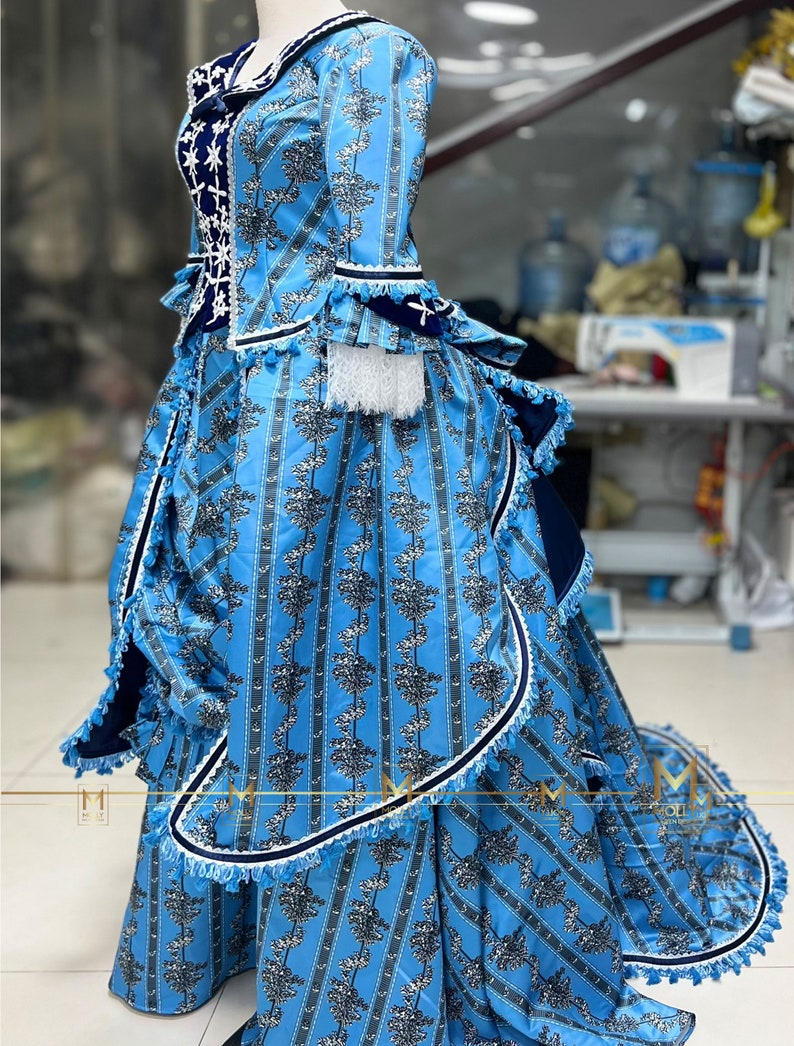 May include: A blue and white patterned dress with a ruffled skirt and a fitted bodice. The dress has a white lace trim and a blue velvet sash.