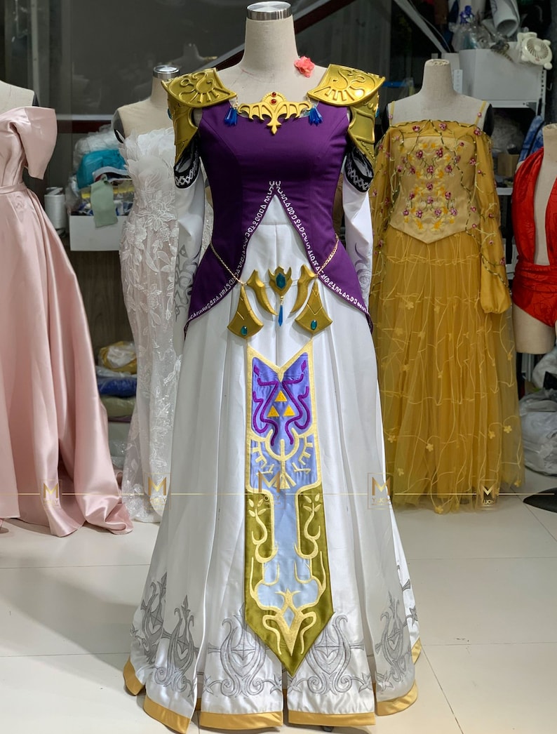 May include: A white and purple princess costume with gold accents and intricate embroidery. The dress features a long skirt, a fitted bodice, and a high neckline. The costume is inspired by a popular video game character.