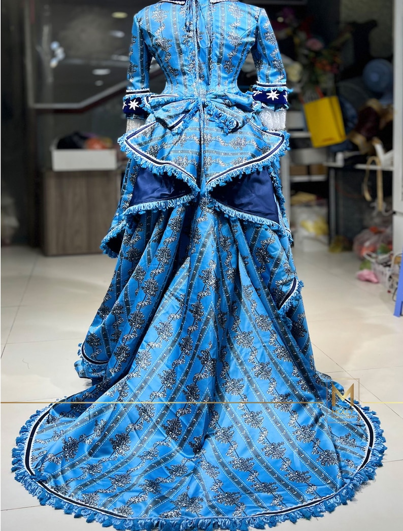 May include: A blue and white patterned dress with a long skirt and a fitted bodice. The dress has a white lace trim and a blue sash. The skirt is full and flowing, and the dress is perfect for a formal occasion.