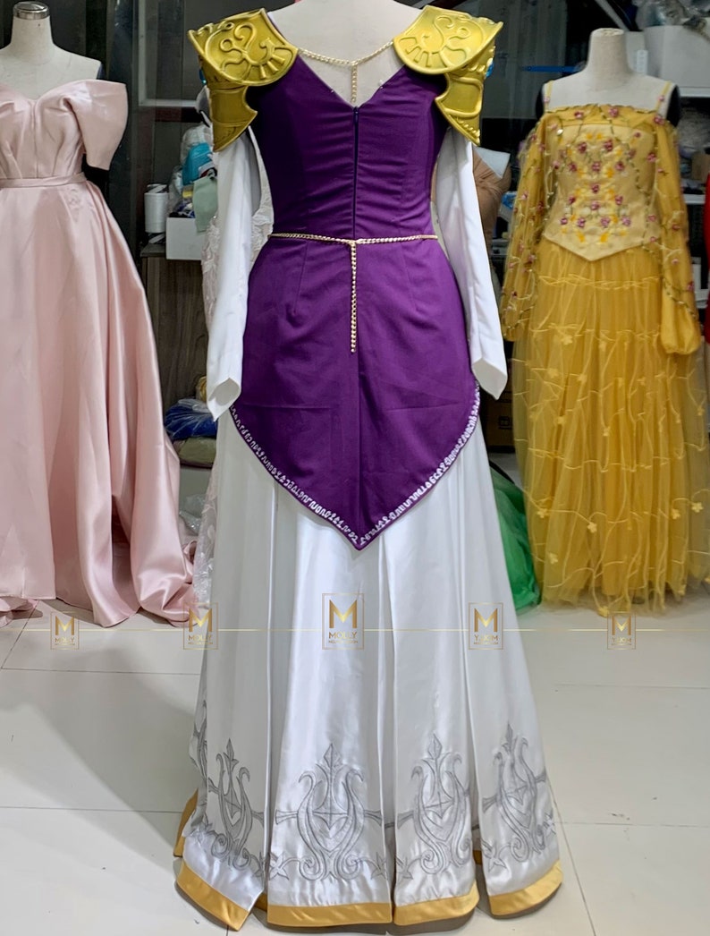 May include: A white and purple princess costume with gold accents. The dress has a white skirt with a gold trim and a purple bodice with gold shoulder pads. The bodice is decorated with rhinestones.